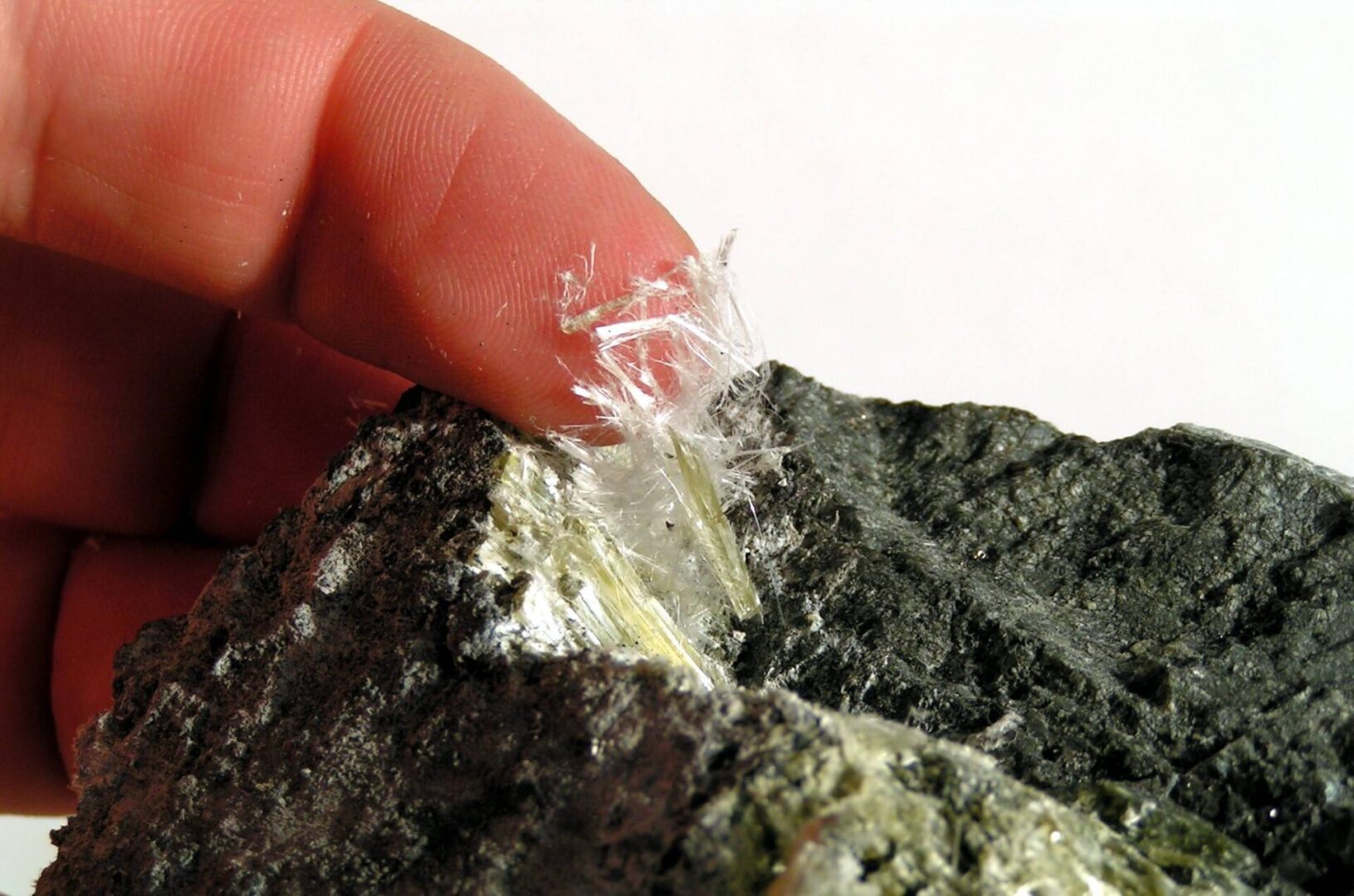 Here's an alt tag for the image: Finger touching asbestos fibers in rock.